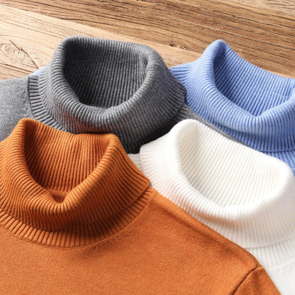 Vier Rollkragenpullover aus Strick in Grau, Blau, Weiß und Orange auf Holztisch.