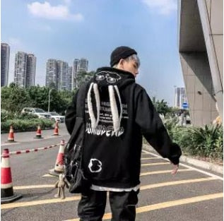 Mann in schwarzem Hoodie mit Engelsflügeln, Stadt im Hintergrund, modisch, urbaner Stil.