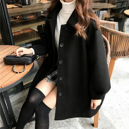 Frau in schwarzem Wollmantel, Rollkragenpullover, karierter Rock, sitzt im Café.