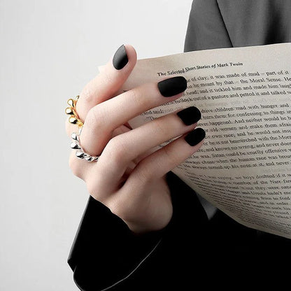 Frau mit schwarzem Nagellack hält Buch, trägt goldene und silberne Ringe, eleganter Look.