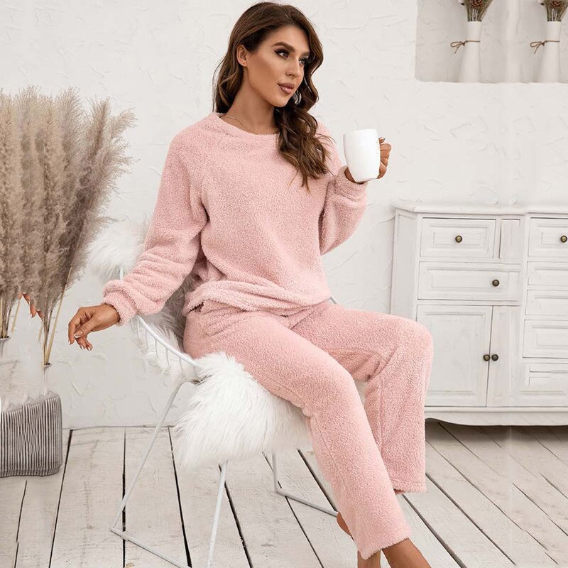 Frau in rosa Fleece-Pyjama mit Tasse, sitzt auf Stuhl, gemütliche Winterkleidung, Wohnzimmer.