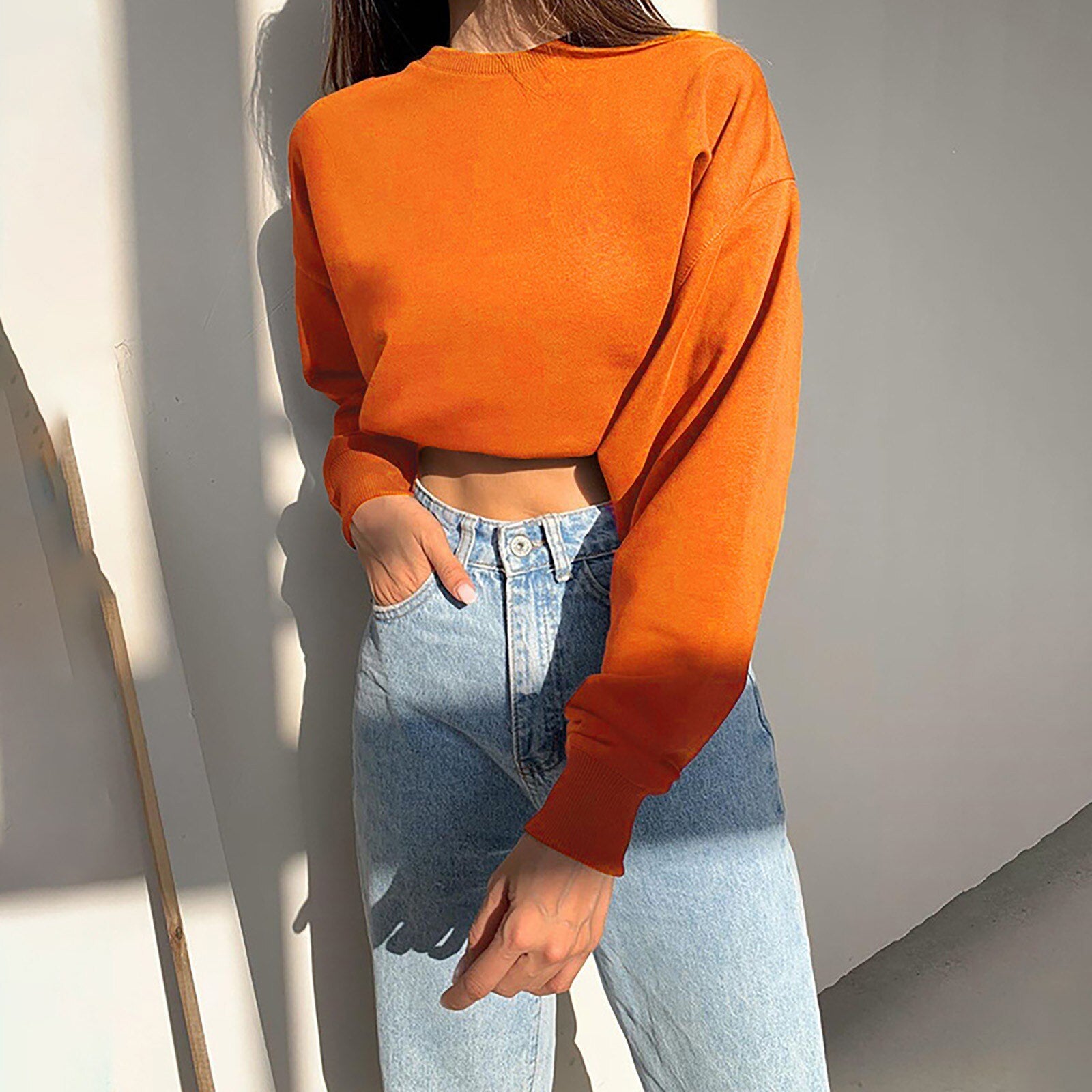 Frau in orangefarbenem Crop-Top und blauer Jeans, lässige Mode, Herbstoutfit.