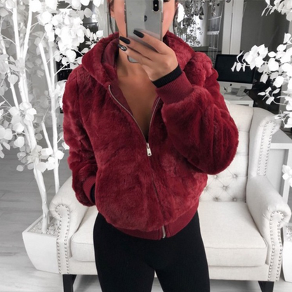 Frau in roter Kunstpelzjacke mit Kapuze, stehend vor weißem Sofa, modisch, gemütlich.