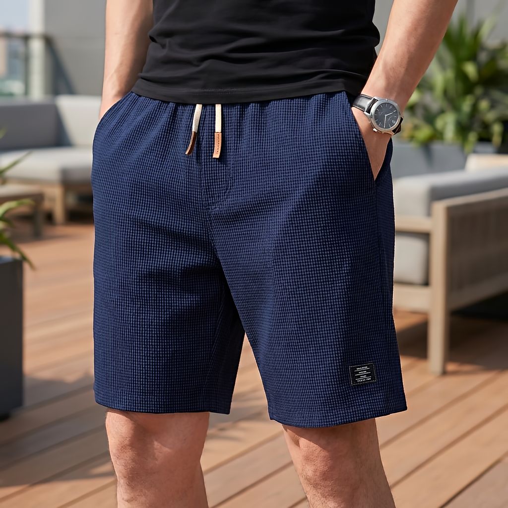 Marinblå shorts i vaffeltyg med vit dragsko och läderdetaljer, burna med en svart t-shirt på en terrass. 7