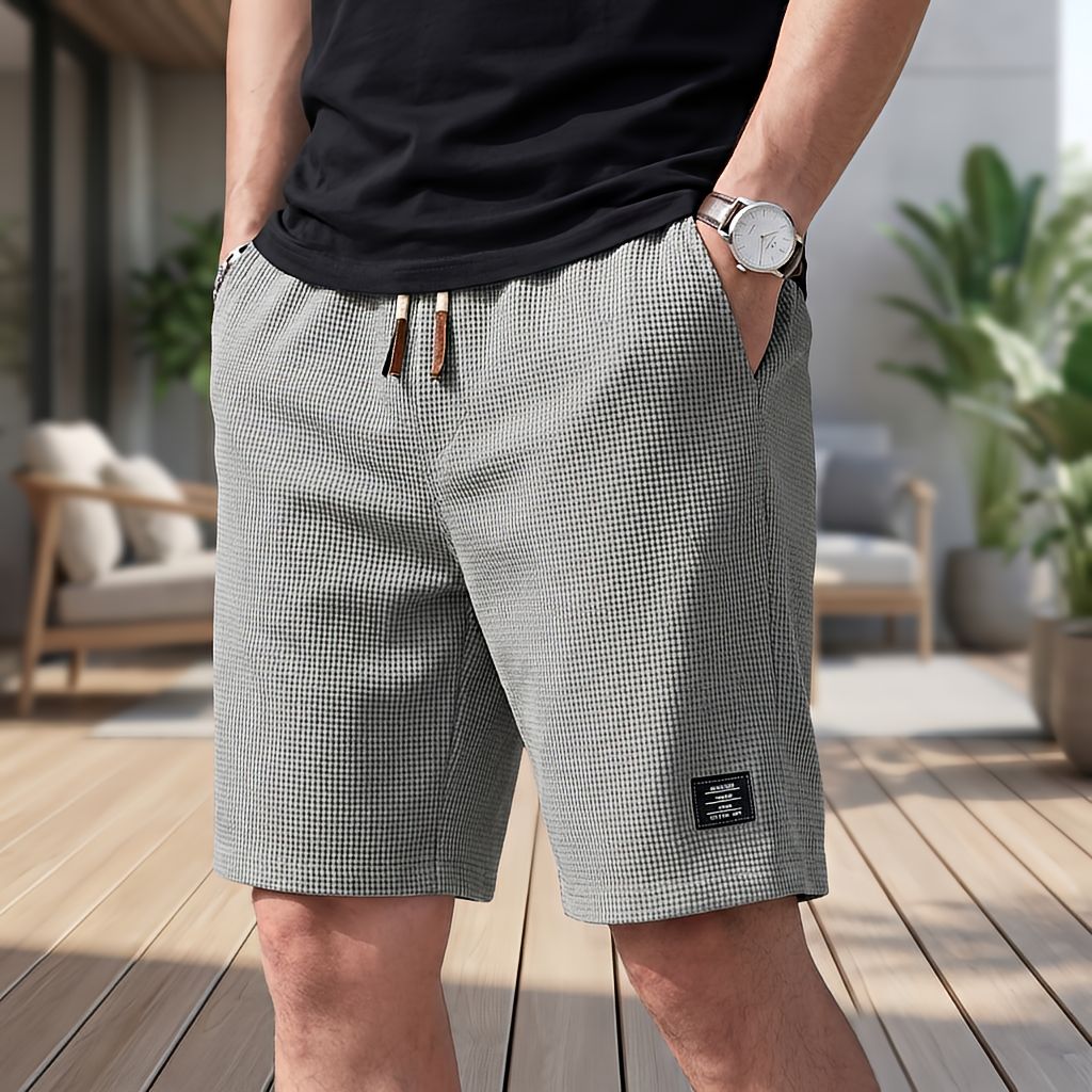 Gråa shorts i vaffeltyg med dragsko i midjan, burna med handen i fickan på en träterrass med loungemöbler. 6