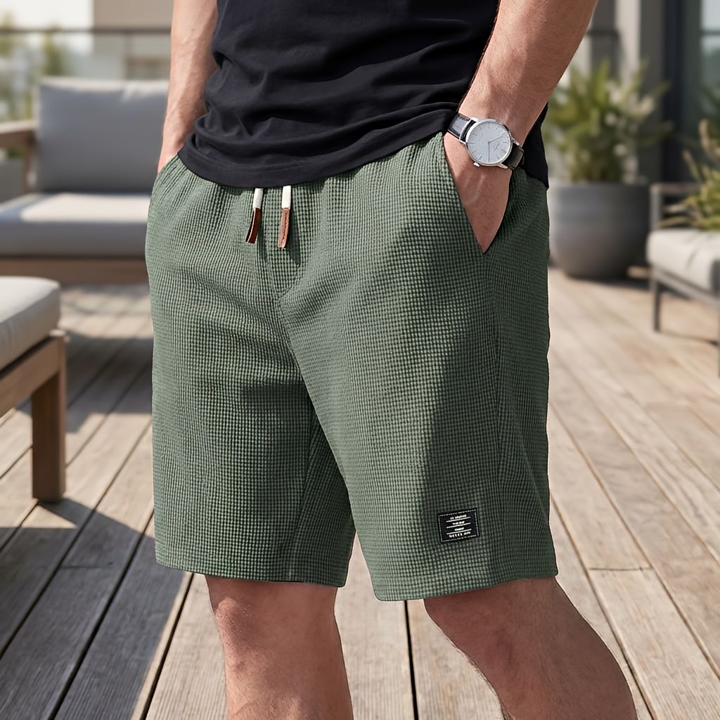 Gröna shorts i vaffeltyg med vit dragsko, burna av en man med armbandsur på en solig trädäck. 5