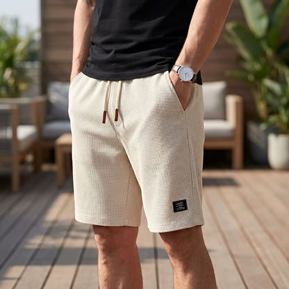 Beige shorts i vaffeltyg med dragsko, burna av en man med armbandsur och handen i fickan på en trädäck. 8