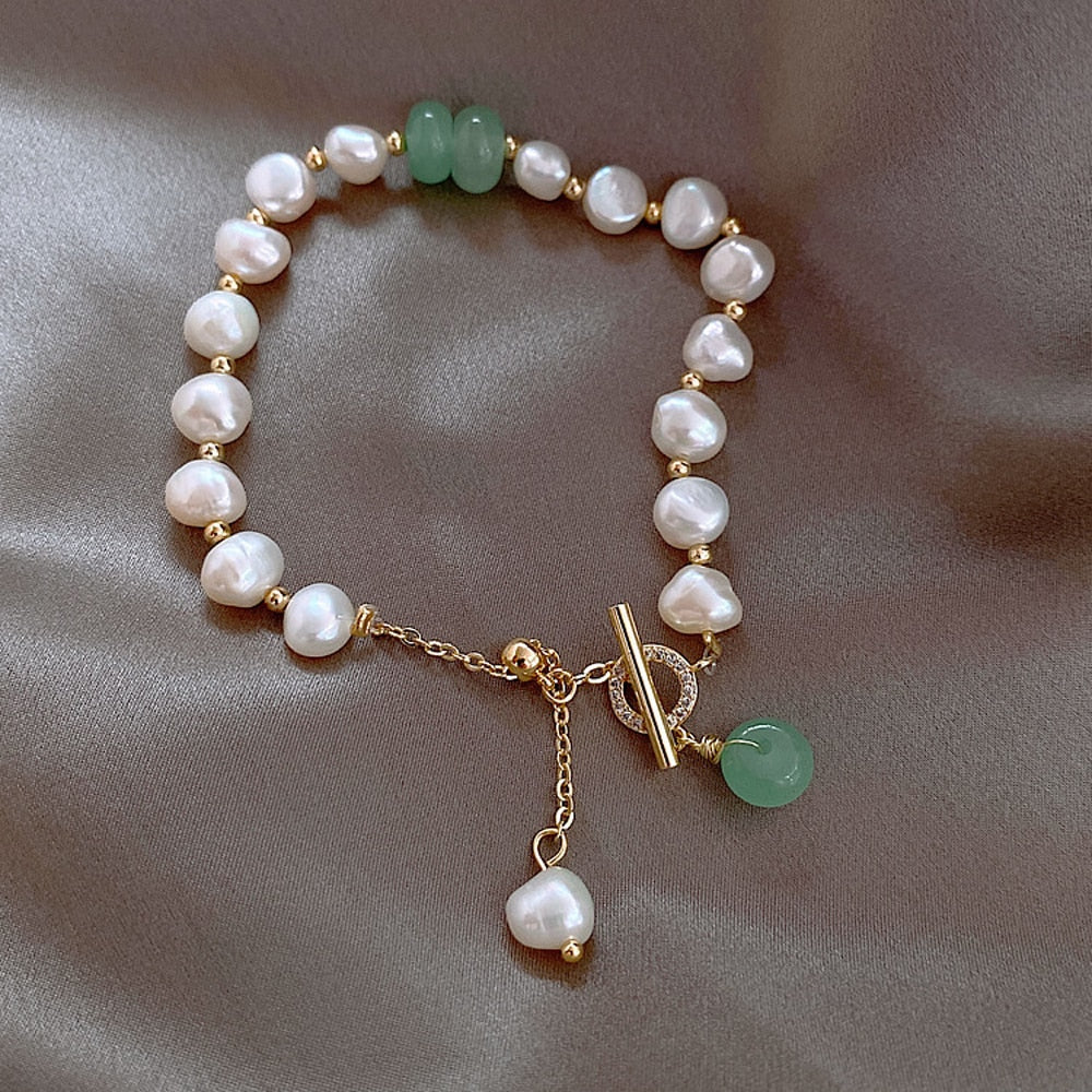 Perlenarmband mit grünen Edelsteinen, goldener Verschluss, eleganter Schmuck auf Seidenstoff.