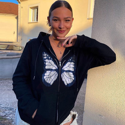Frau in schwarzem Hoodie mit Schmetterlingsmotiv, lächelnd, draußen bei Sonnenuntergang.