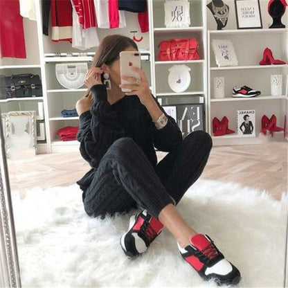 Frau in schwarzem Pullover und Jogginghose, trägt rot-weiße Sneaker, sitzt auf weißem Teppich.
