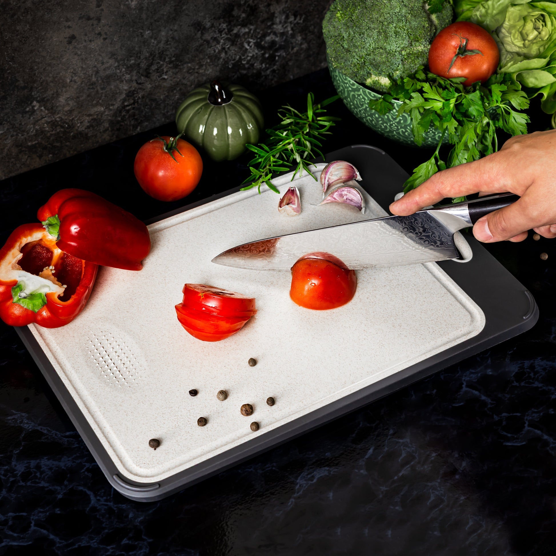 Küchenmesser schneidet Tomaten auf Schneidebrett, umgeben von Paprika und Gemüse.