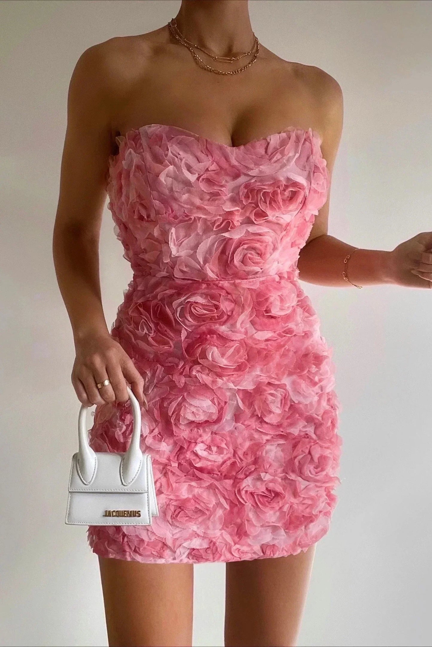 Frau im rosa Blumenkleid mit weißer Mini-Handtasche, elegantes Abendoutfit.