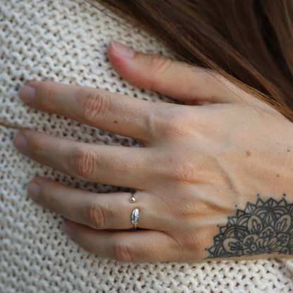 Silberner Verstellbarer Ring mit Blattdesign auf tätowierter Hand, gestrickter Hintergrund.