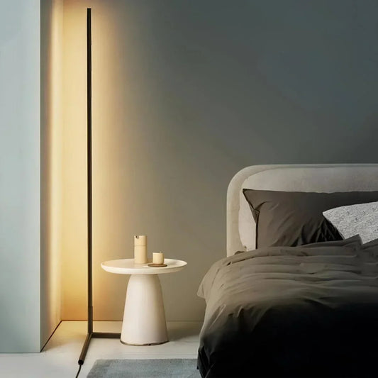 Tänd golvlampa med varmt sken bredvid ett vitt sidobord och en säng med mörkt sänglinne 1