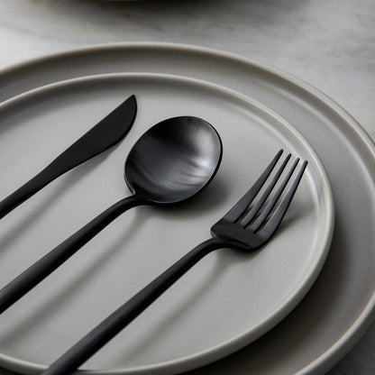 Schwarzes Besteck-Set auf grauem Teller, modernes Design, Edelstahl, Essbesteck.
