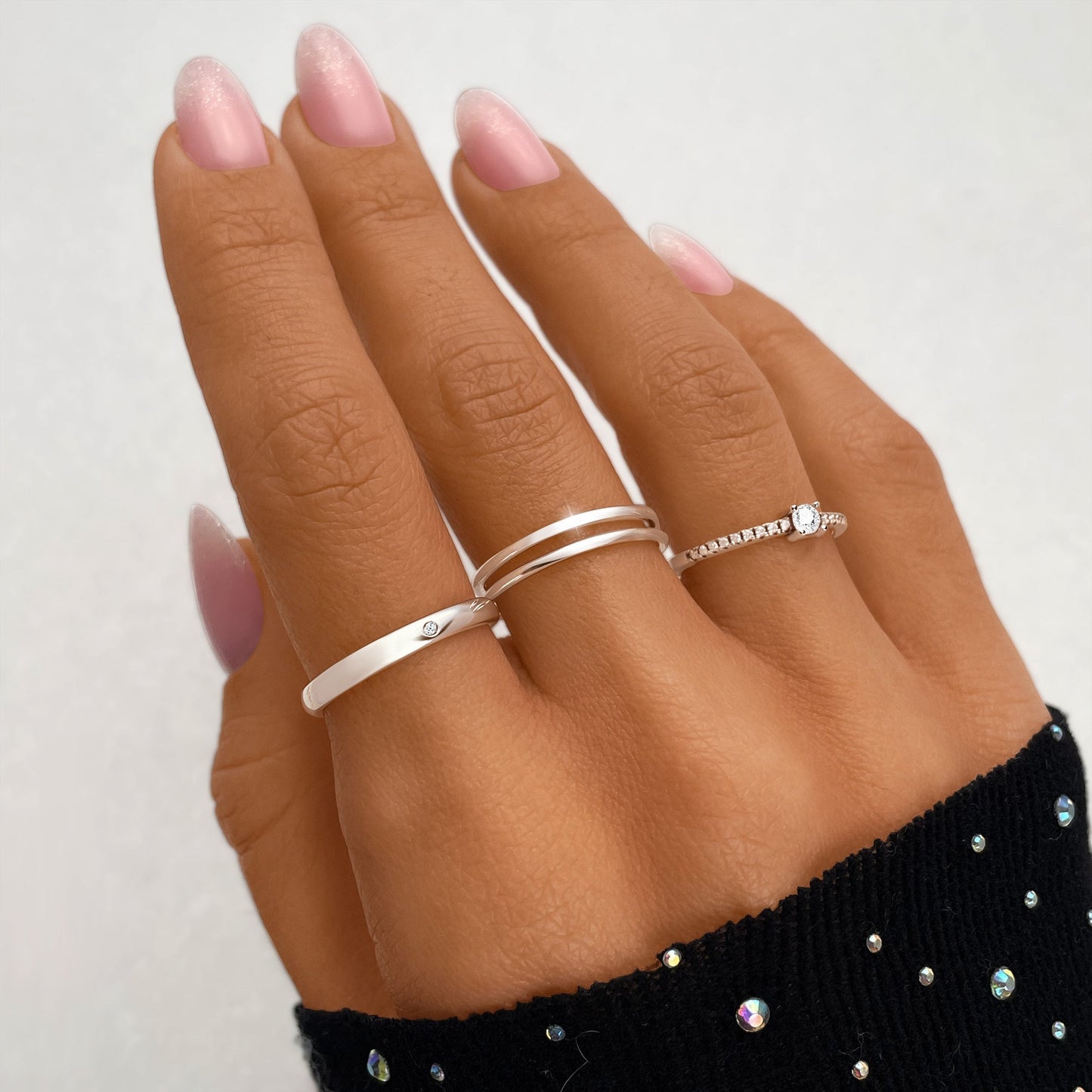 Drei silberne Ringe an Hand mit rosa Nägeln, elegantes Design, Schmuckmode, Damenaccessoires.