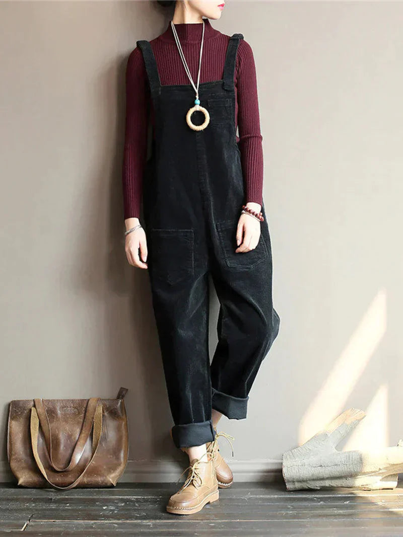 Frau in schwarzem Cord-Overall, rotem Pullover, braunen Stiefeln, braune Ledertasche.