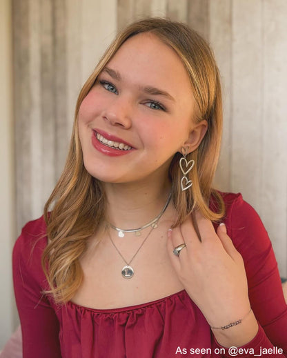 Frau trägt silberne Herz-Ohrringe, rotes Oberteil, lächelt, modisches Accessoire, Schmuck.