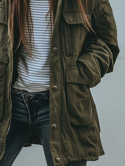 Detaljbild av tryckknappsslutning och stora framfickor med lock på jackans högra sida, buren över randig topp och jeans. 3