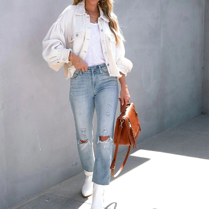 Frau in weißer Jeansjacke, zerrissener Jeans und weißen Stiefeln mit brauner Ledertasche.