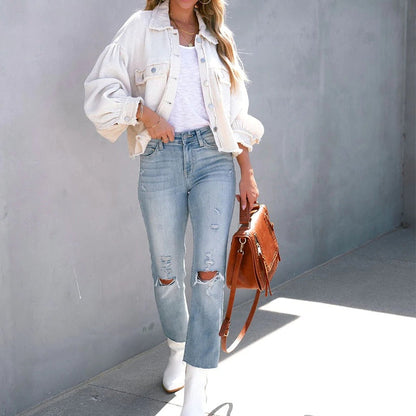 Frau in weißer Jeansjacke, zerrissener Jeans und weißen Stiefeln mit brauner Ledertasche.