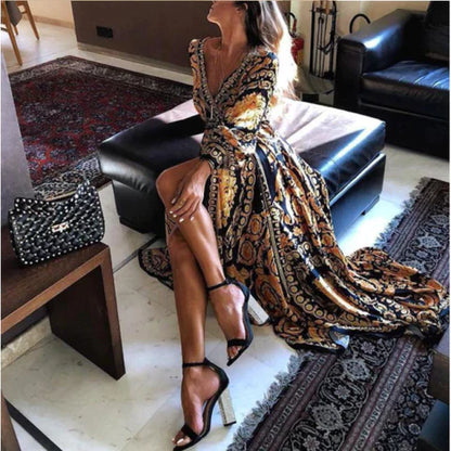 Frau in gelbem, schwarzem Maxikleid mit Muster, sitzt auf Sofa, elegante Sandalen.