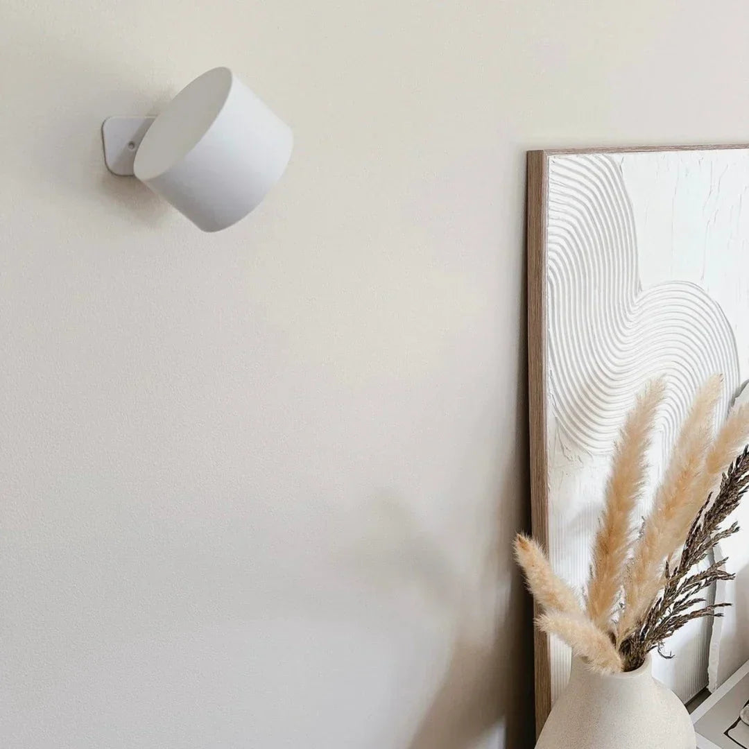 Släckt vit vägglampa på ljus vägg bredvid en inramad tavla och en vas med pampasgräs 16