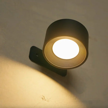 Svart vägglampa med ringmönstrat ljusfönster lyser varmt och kastar en ljuscirkel på väggen 3
