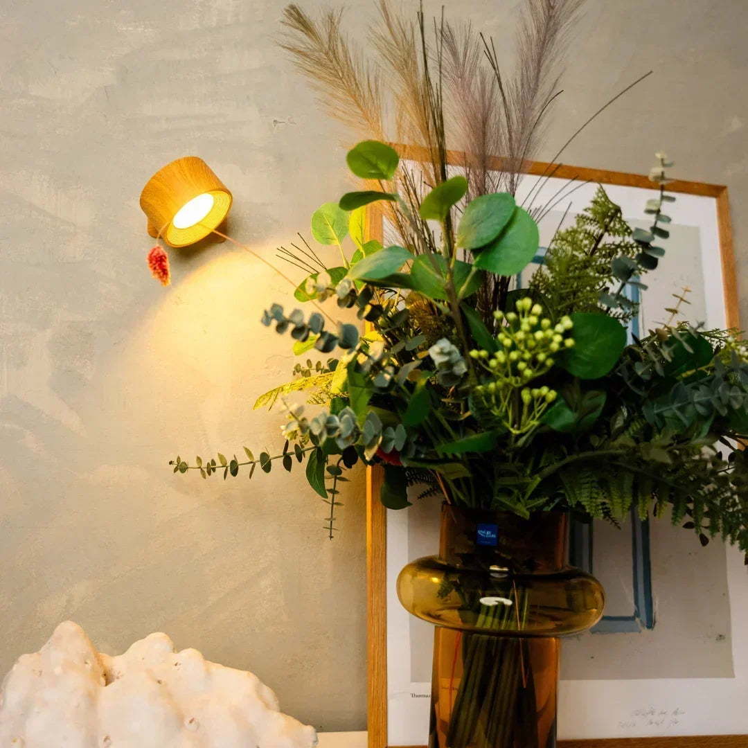 Vägglampa i träfinish lyser över en vas med torkade blommor och eukalyptus 5