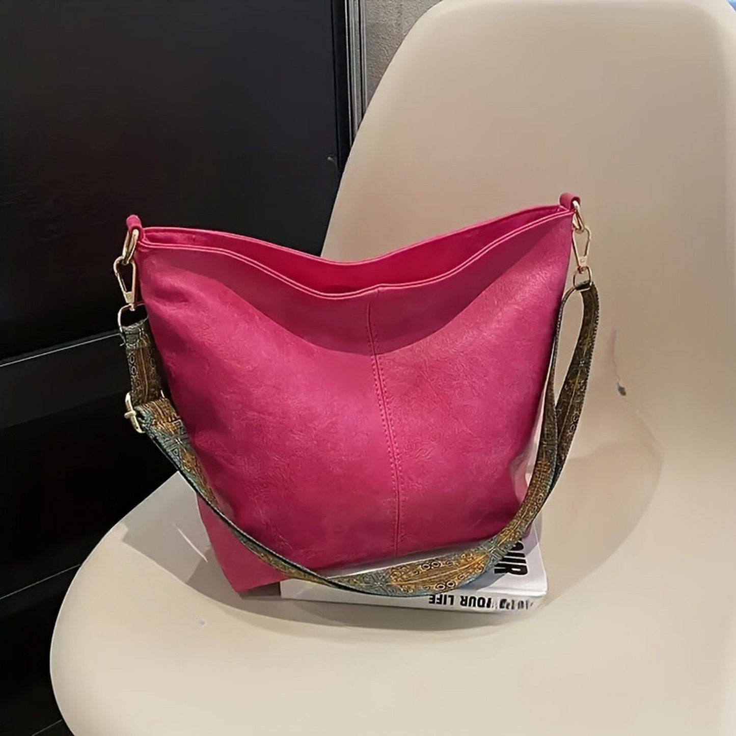 Rosa Damenhandtasche aus Leder mit verstellbarem Riemen auf einem Stuhl.