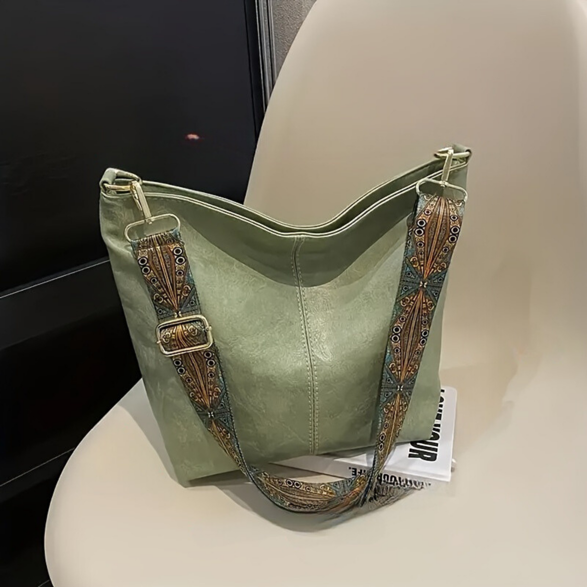 Grüne Ledertasche mit verziertem Schultergurt auf einem Stuhl, modisches Accessoire.