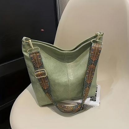 Grüne Ledertasche mit verziertem Schultergurt auf einem Stuhl, modisches Accessoire.