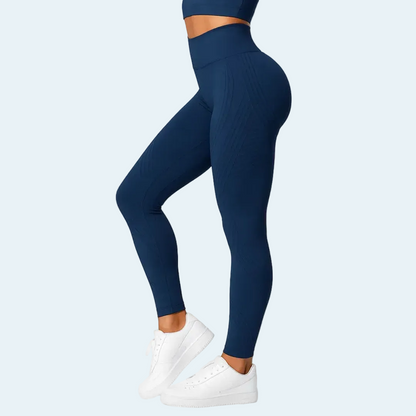 Marinblå tights med högt linne i midjan, sedda från sidan på en modell som står på tå i vita sneakers. 4
