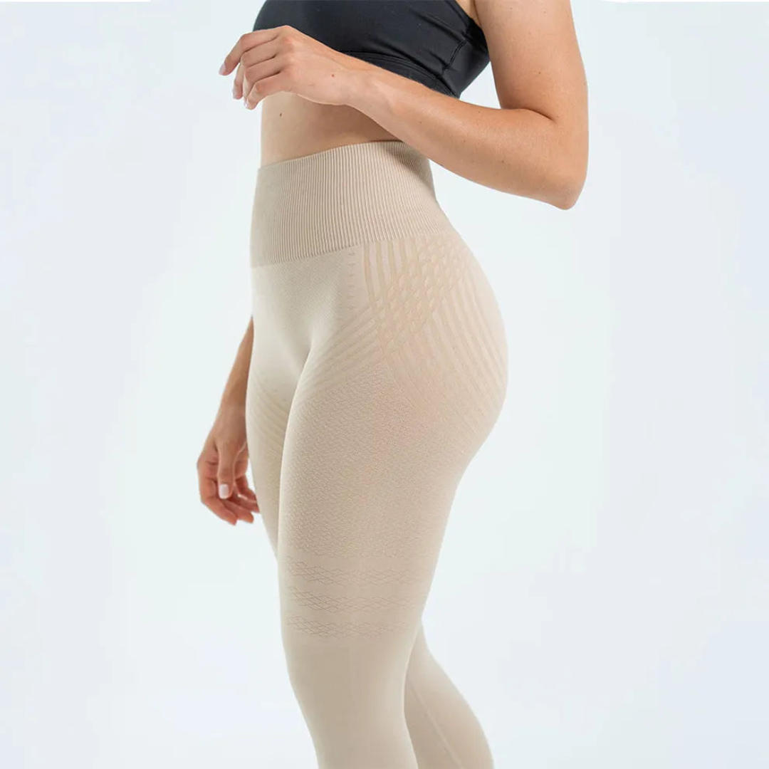 Beige tights med brett ribbat midjeband och diagonala mönsterränder, sedda från sidan på en modell i svart sport-bh. 2