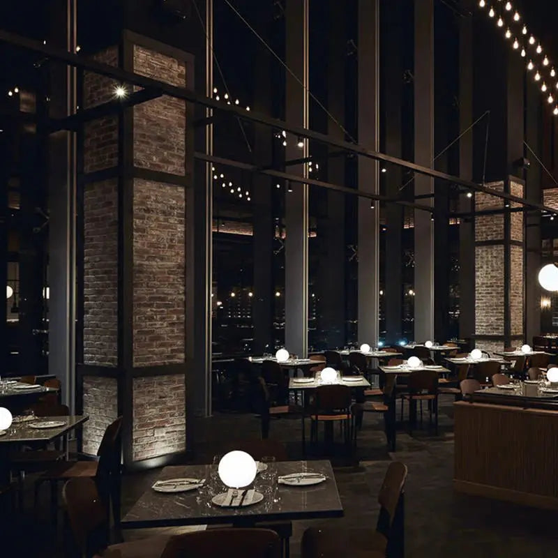 Rustik restauranglokal med tegelpelare och mörka bord, där flera lysande vita klotlampor står som bordsbelysning. 8