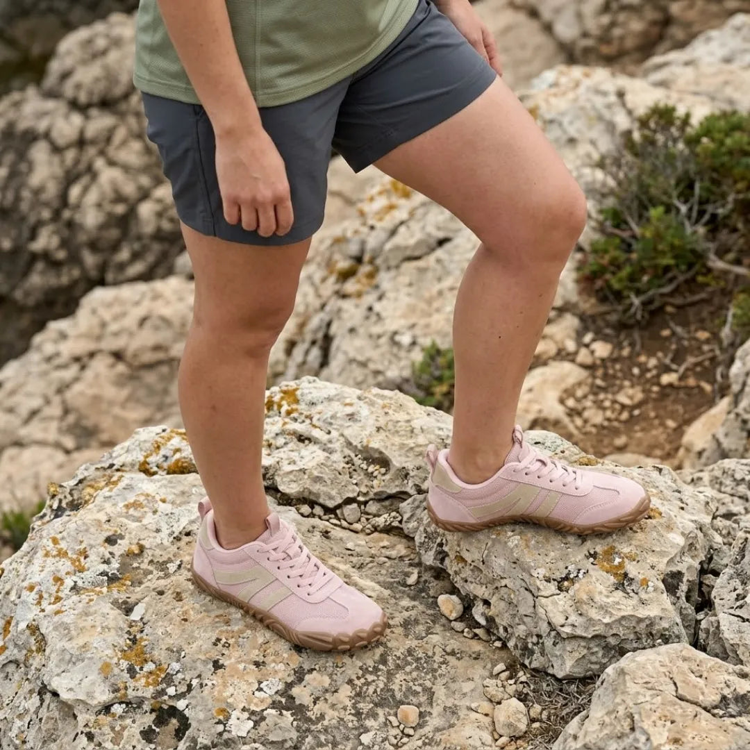 Person i shorts och grön topp står på klippor med rosa skor med beige ränder och brun sula. 11
