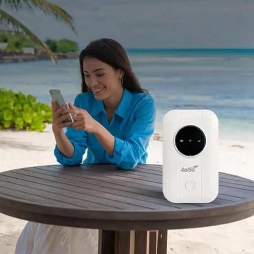 Leende kvinna använder mobilen vid ett runt bord på en strand, med vit router bredvid 6