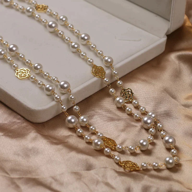 Lange Perlenkette mit goldenen Rosendetails auf beigem Stoff, eleganter Schmuck für Damen.
