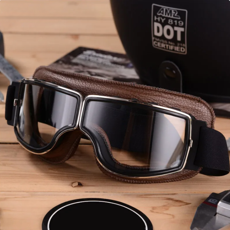 Braune Vintage-Motorradbrille mit Lederrahmen auf Holztisch, ideal für Retro-Look.