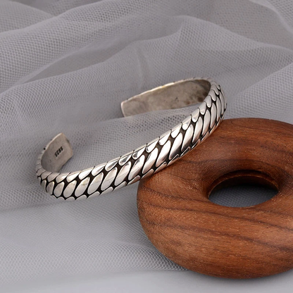 Silberarmreif mit Fischgrätenmuster auf Holz und Stoff, eleganter Schmuck für Damen.