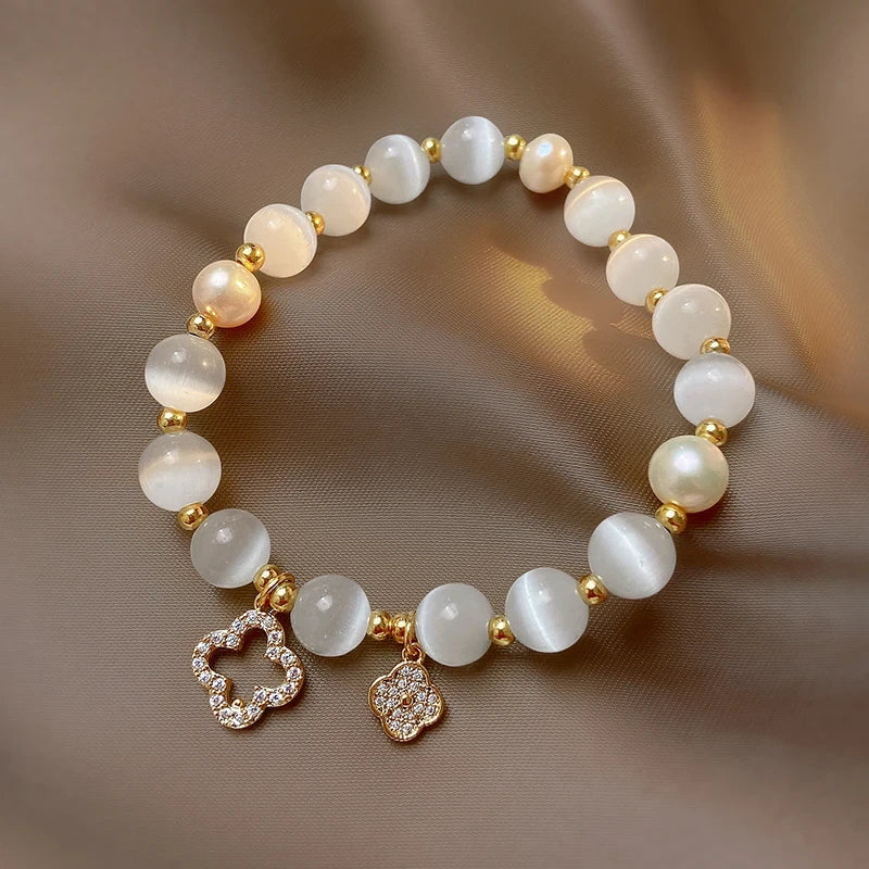 Armband aus weißen Perlen mit goldenen Akzenten und Blumenanhängern, eleganter Schmuck.