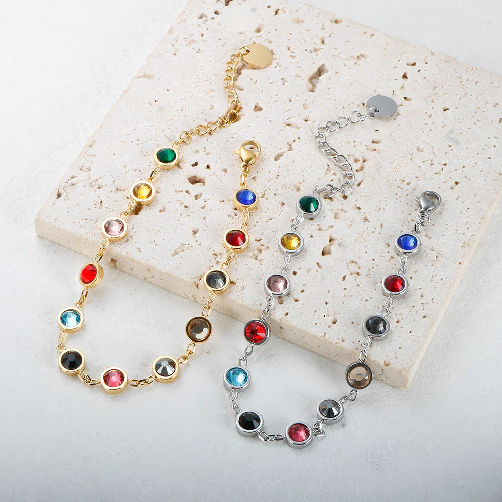 Armbänder mit bunten Kristallen auf Steinplatte, goldene und silberne Ketten, modischer Schmuck.