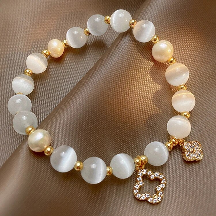 Perlenarmband mit weißen Perlen, goldenen Akzenten und funkelndem Blumenanhänger auf braunem Hintergrund.