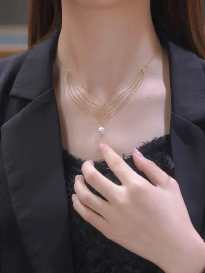 Frau mit elegantem goldenen Halskette, schwarzes Kleid, Hand zeigt auf Perlenanhänger.