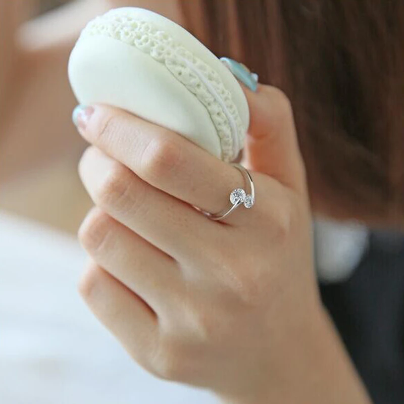 Frau hält weißen Macaron, trägt silbernen Ring mit Kristall, Nahaufnahme, elegante Hand.