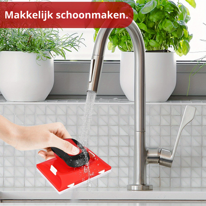 Rote Reinigungsschwamm mit Griff, Küche, Wasserhahn, leicht zu reinigen, Pflanzen im Hintergrund.