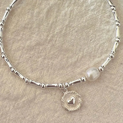 Silberarmband mit Perle und Herzanhänger, elegantes Schmuckdesign, Damenaccessoire.