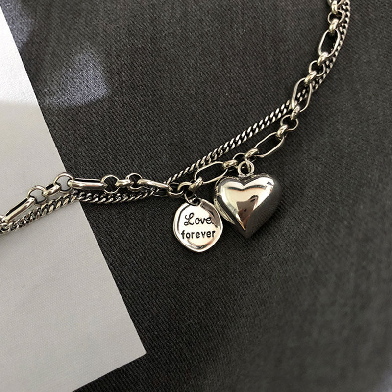 Silberarmband mit Herzanhänger und "Love forever"-Gravur auf grauem Hintergrund.