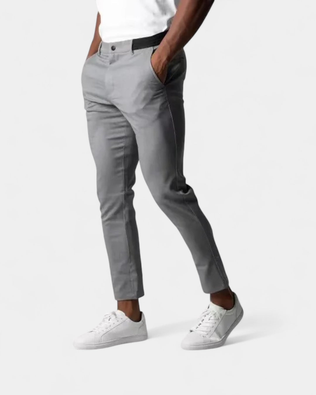 Man i vit t-shirt och vita sneakers bär grå byxor med handen i fickan 1