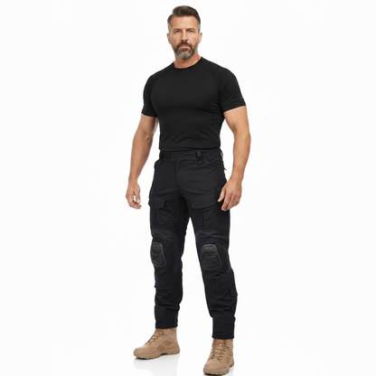 Skäggig man i helfigur, svart tröja och beige kängor, bär de svarta byxorna sedda framifrån. 7